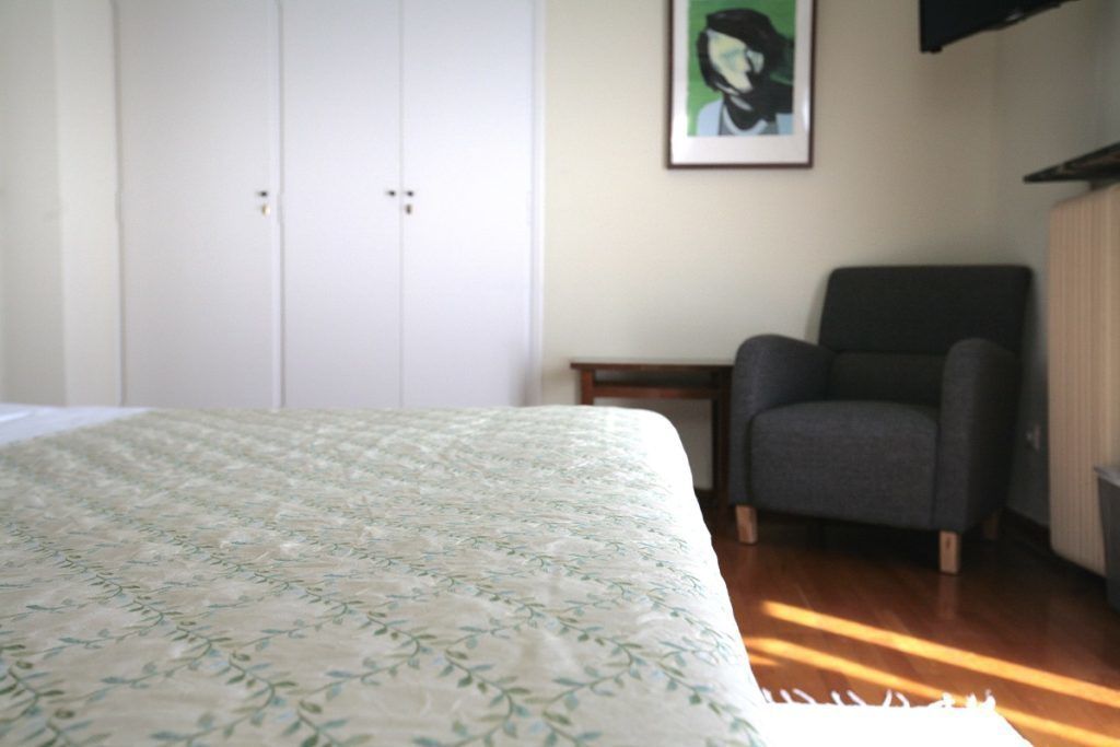 A bedroom with a bed, a chair, a wardrobe, and a painting on the wall.