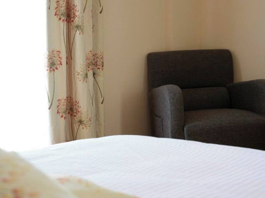 Quarto de hotel com uma cama, uma poltrona cinzenta e cortina com padrão floral.