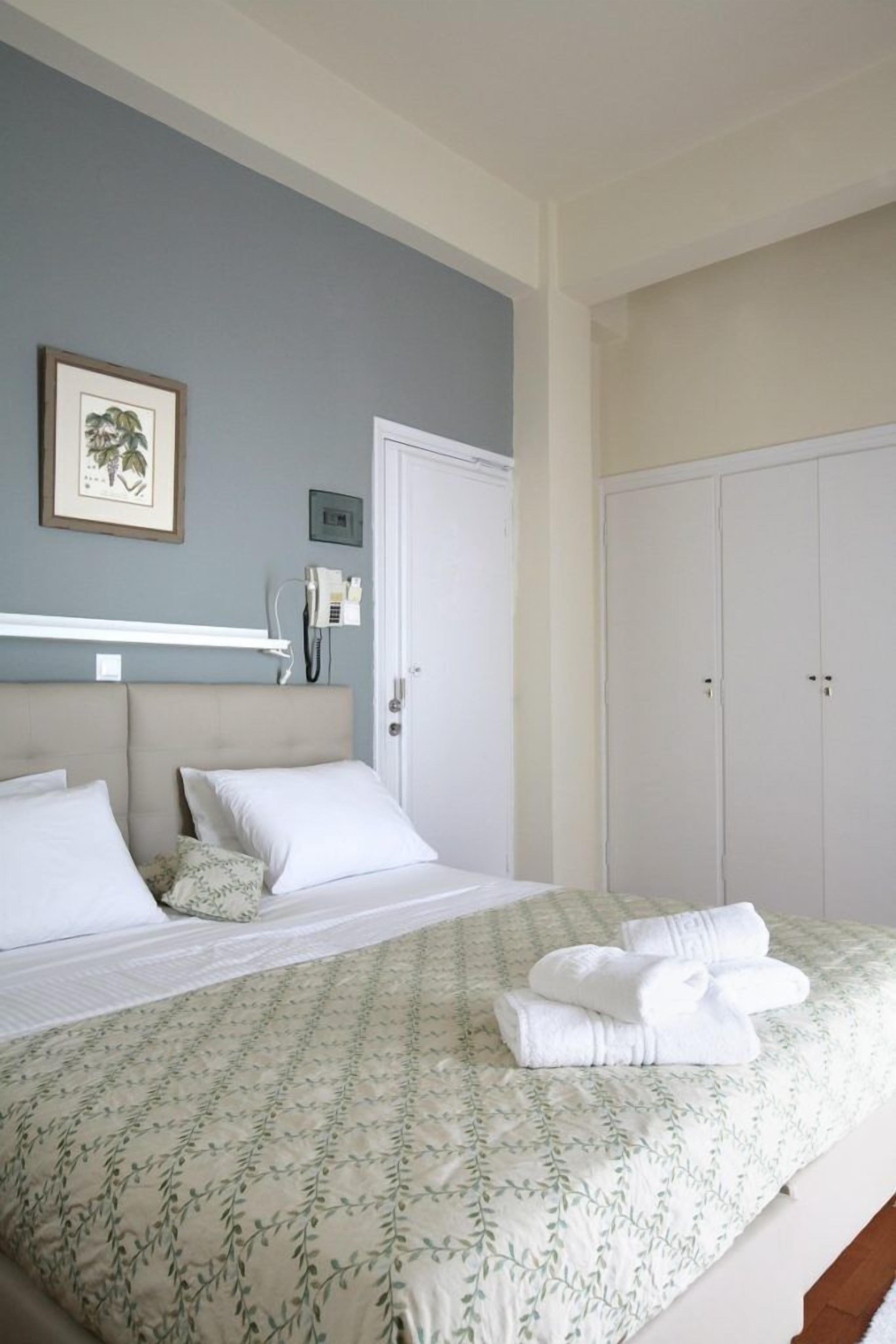 A bedroom with a bed, a wardrobe, a framed picture on the wall, and a telephone on a shelf.