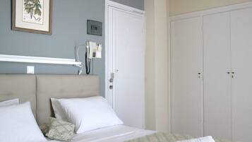 A bedroom with a bed, a wardrobe, a framed picture on the wall, and a telephone on a shelf.