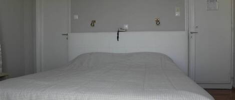 A bedroom with a single bed, two doors, and a small wall-mounted light fixture.