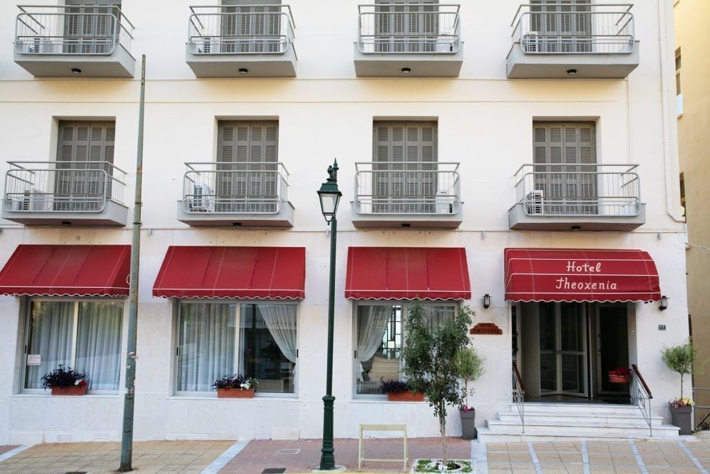Un hotel con balcones, toldos rojos y un letrero que dice "Hotel Theoxenia".