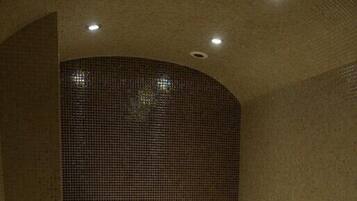 A sauna room with a bench, a small sink, and a tiled wall.