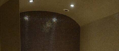 Una sala de sauna con banco, un lavamanos pequeño y pared de azulejos.