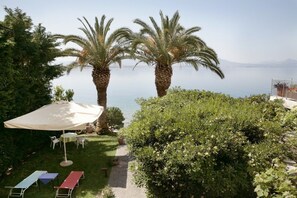 A patio with a table and chairs, palm trees, and a view of the sea. - Hotel Theoxenia (Loutraki-Agioi Theodoroi)