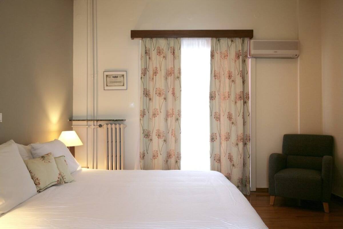 Un dormitorio con cama, una silla, un radiador y cortinas.