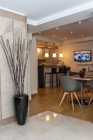 Una cocina moderna con zona de comedor, que presenta un pilar de mármol, un florero negro con ramas y un televisor montado en la pared.