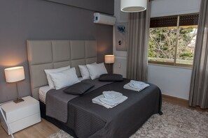 A modern bedroom with a large bed, bedside lamps, a radiator, and a window with curtains. - Urban Residence (Marousi)