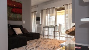 Un salon moderne avec un canapé foncé, un tapis moelleux, un coin repas comprenant une table et des chaises, et une vue sur l’extérieur grâce à de grandes fenêtres.