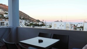 Un balcón con mesa y sillas, con vistas a un pueblo costero de edificios blancos y una colina al fondo.