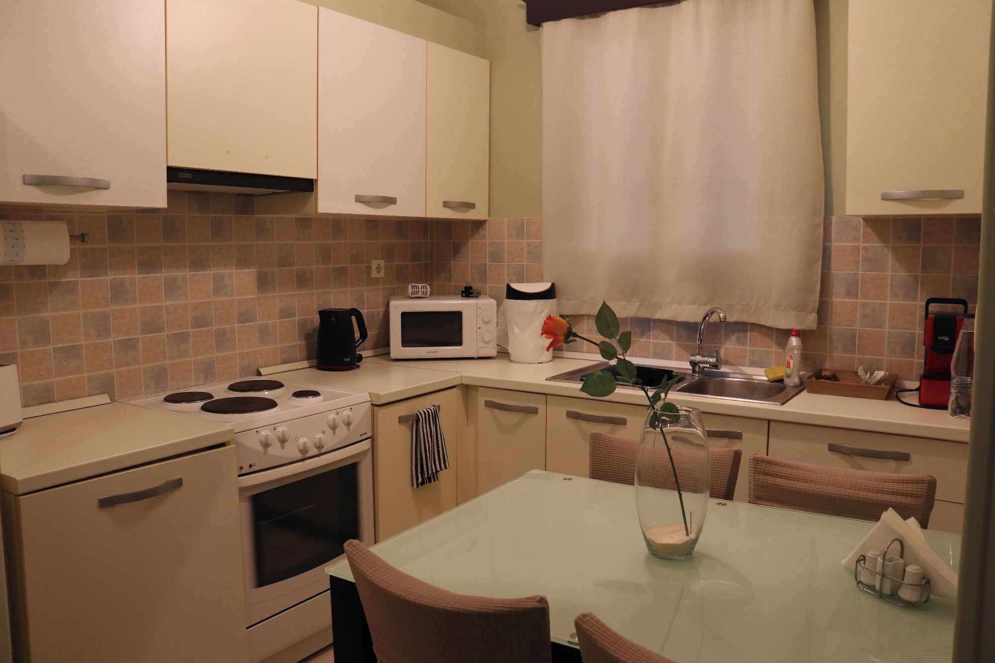 A compact kitchen with a stove, microwave, and sink. There is a dining table with chairs and a vase with a plant.