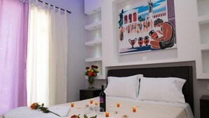 Habitación de hotel con cama, mesita de noche con un florero y un cuadro en la pared, además de velas sobre la cama.