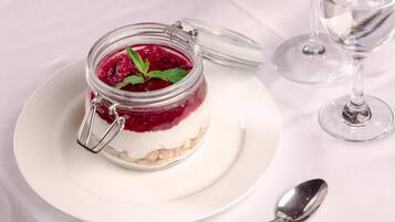 Un postre en un tarro de vidrio con cierre metálico, sobre un plato blanco y con una cuchara a un lado.