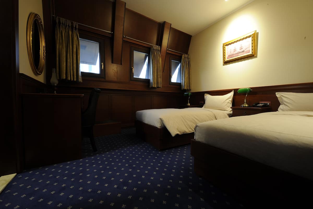 A hotel room with two beds, a desk, a chair, a dresser, and a framed picture on the wall.