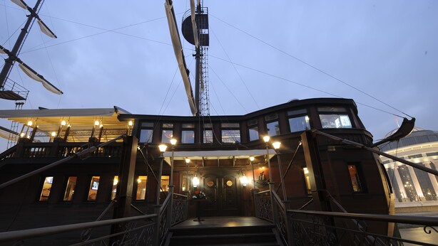 Cubierta de barco con una escalera que conduce a un área cubierta con varias ventanas y barandilla.
