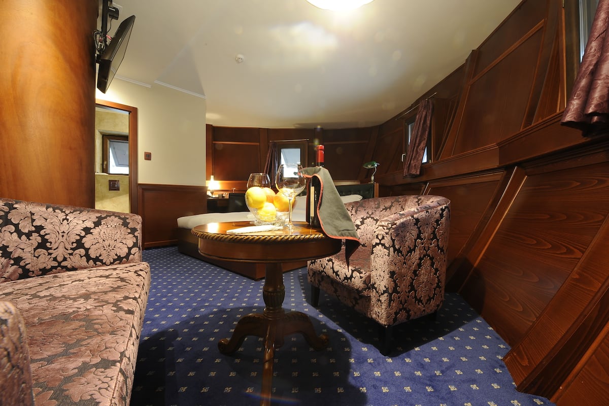 A cozy room with a patterned sofa, a round table with a lamp, and a view through a window.