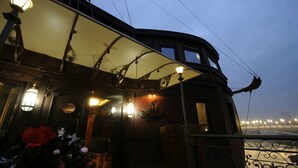 Un restaurante frente al río con terraza al aire libre, iluminado por lámparas colgantes y vistas al río.