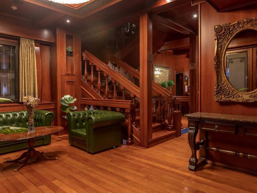 A spacious living room with a green leather sofa, a wooden coffee table, and a staircase leading to an upper floor.