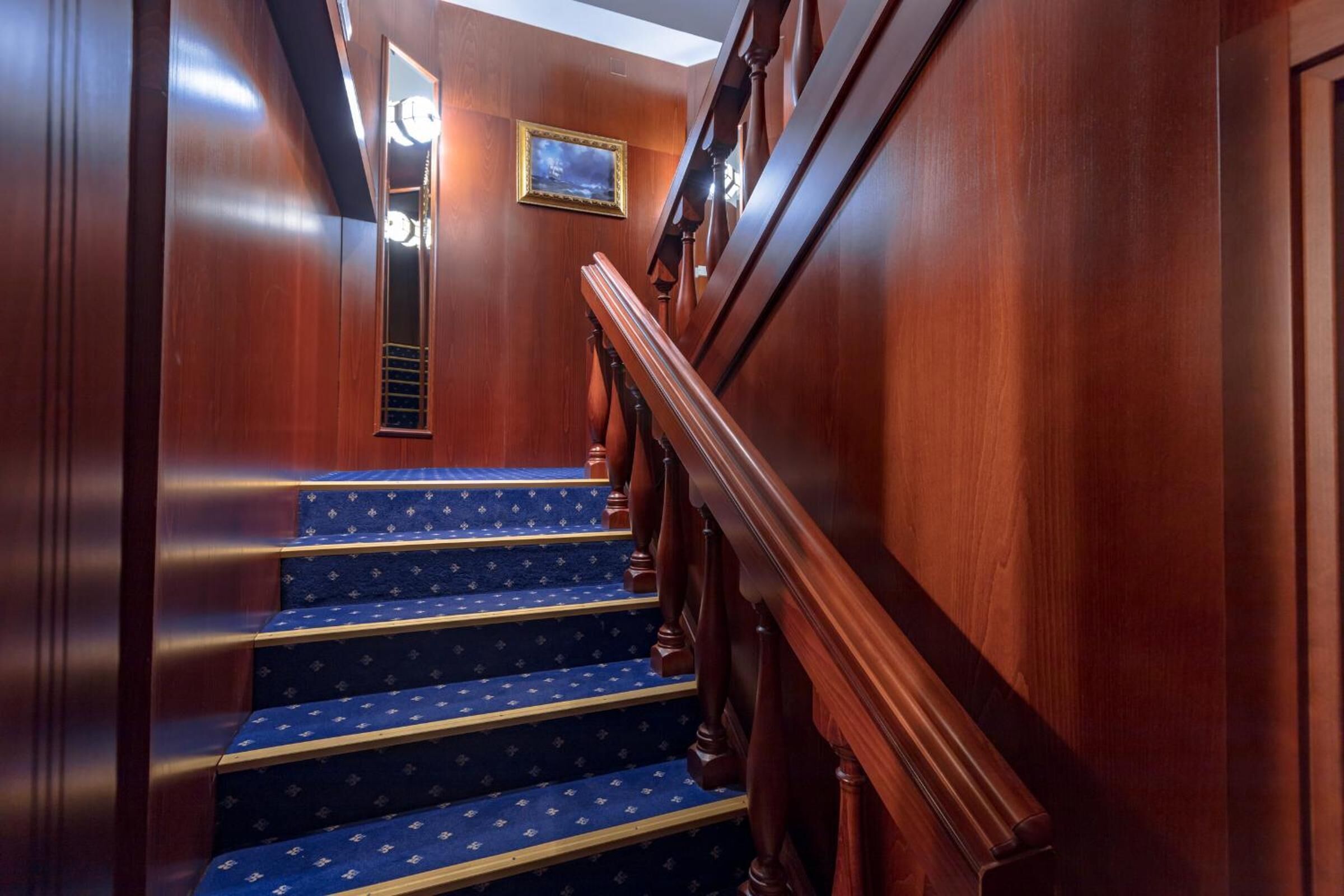 A wooden staircase with blue carpeted steps and a wooden handrail.