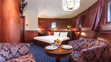 A hotel room with a bed, two armchairs, a small table with plates and fruit, and a chandelier.