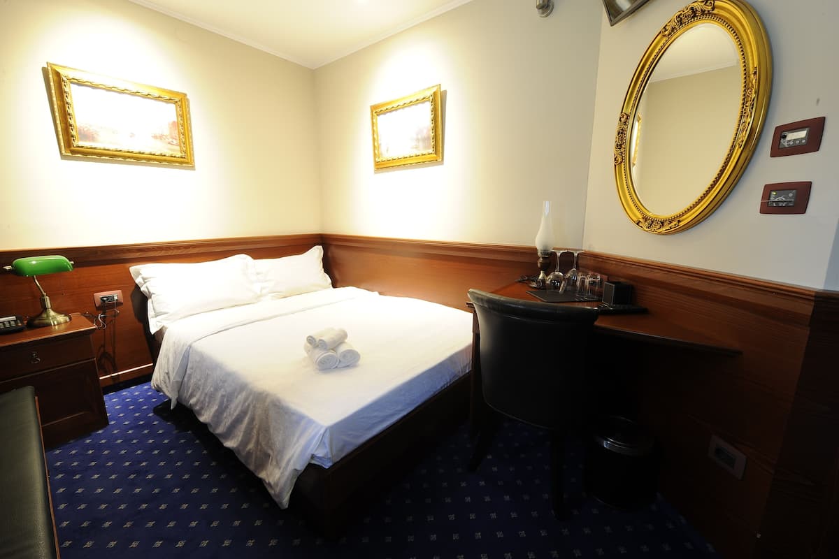 A hotel room with a bed, bedside table, lamp, and a large mirror.