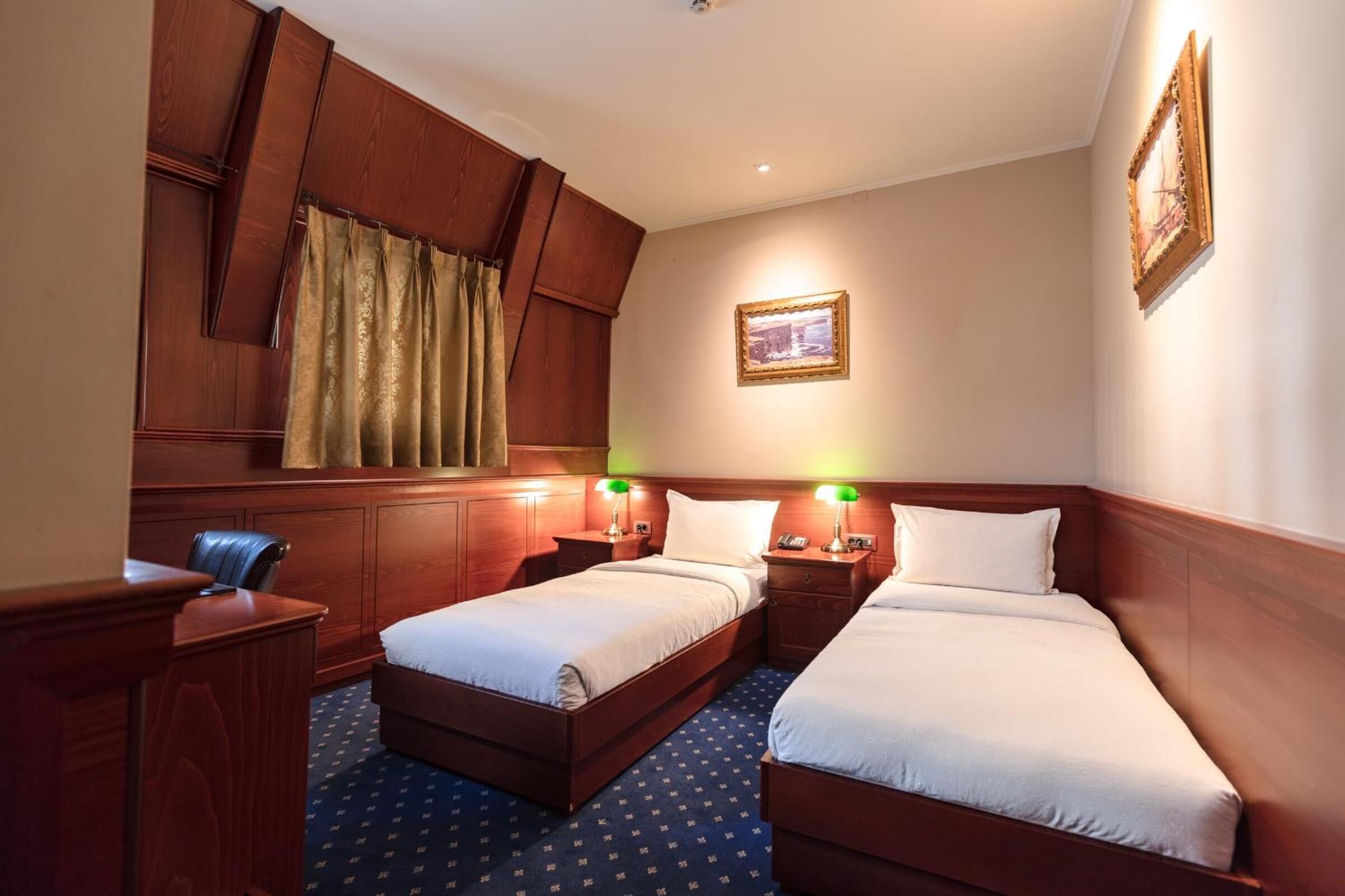 A hotel room with two beds, wooden paneling, a desk, and a chair.