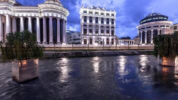A grand building with classical architecture, featuring columns and domes, situated beside a calm river.
