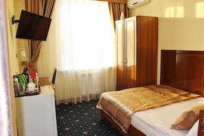 Una habitación de hotel con cama, escritorio con televisor, armario y ventana con cortinas.