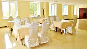 A room with multiple tables and chairs, arranged in rows, with large windows allowing natural light.