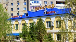 A hotel with a blue roof and yellow walls, featuring arched windows and a visible sign in a foreign language.