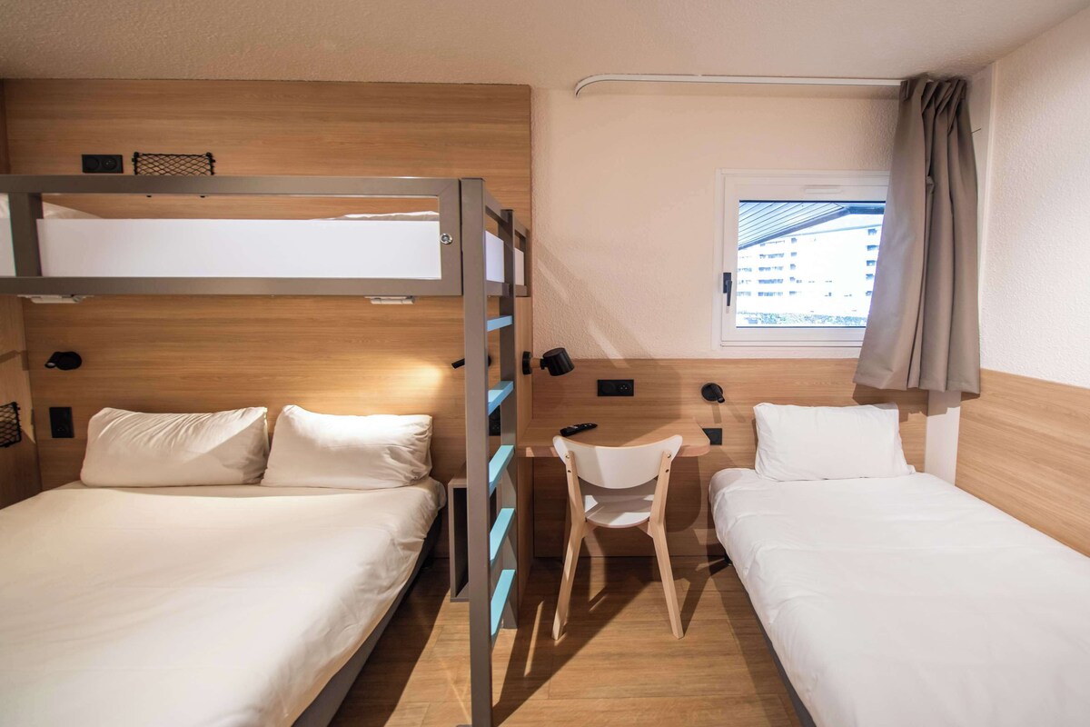 Een kleine hotelkamer met twee bedden, een bureau en een stoel.