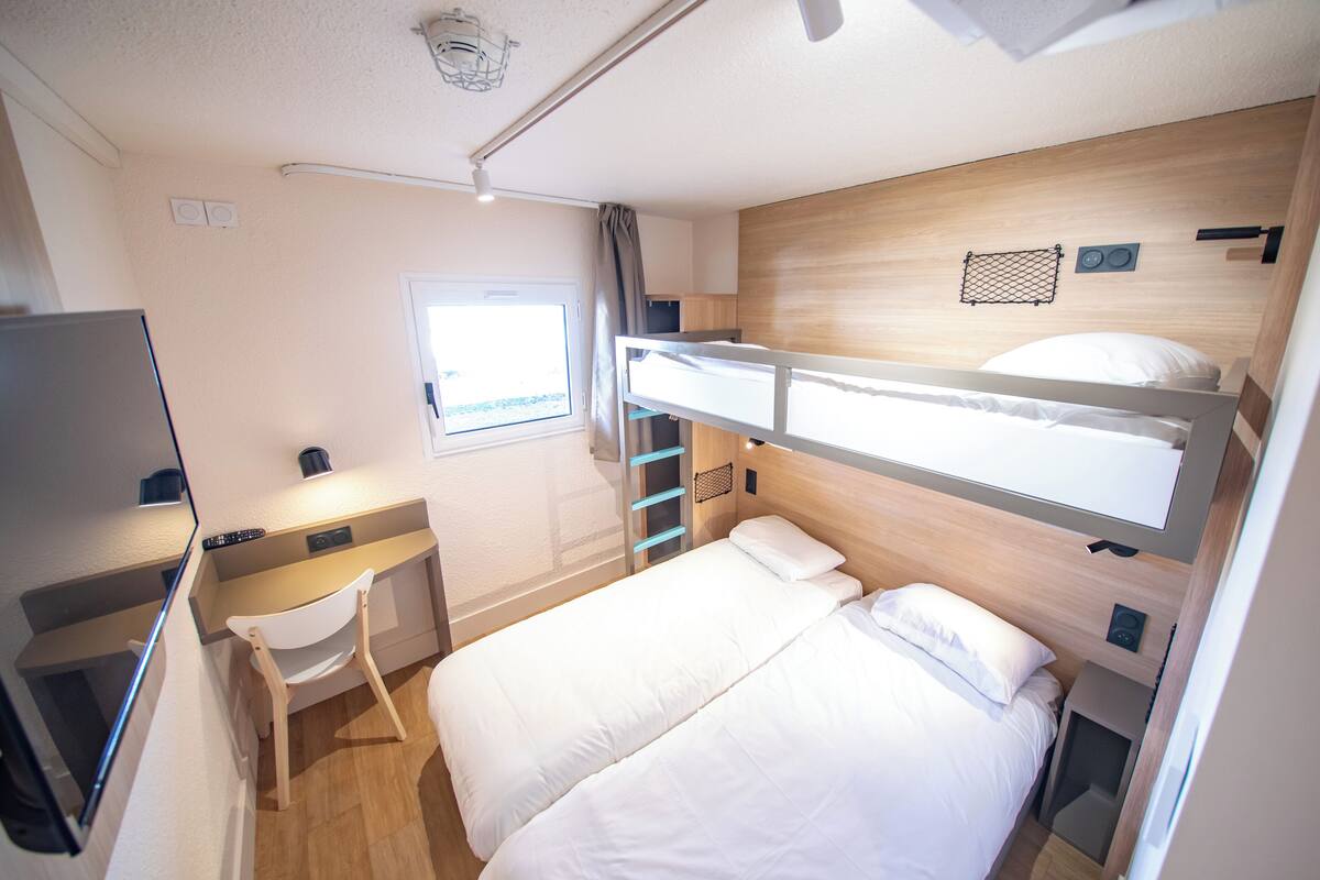 Habitación de hotel pequeña con literas, escritorio y ventana.