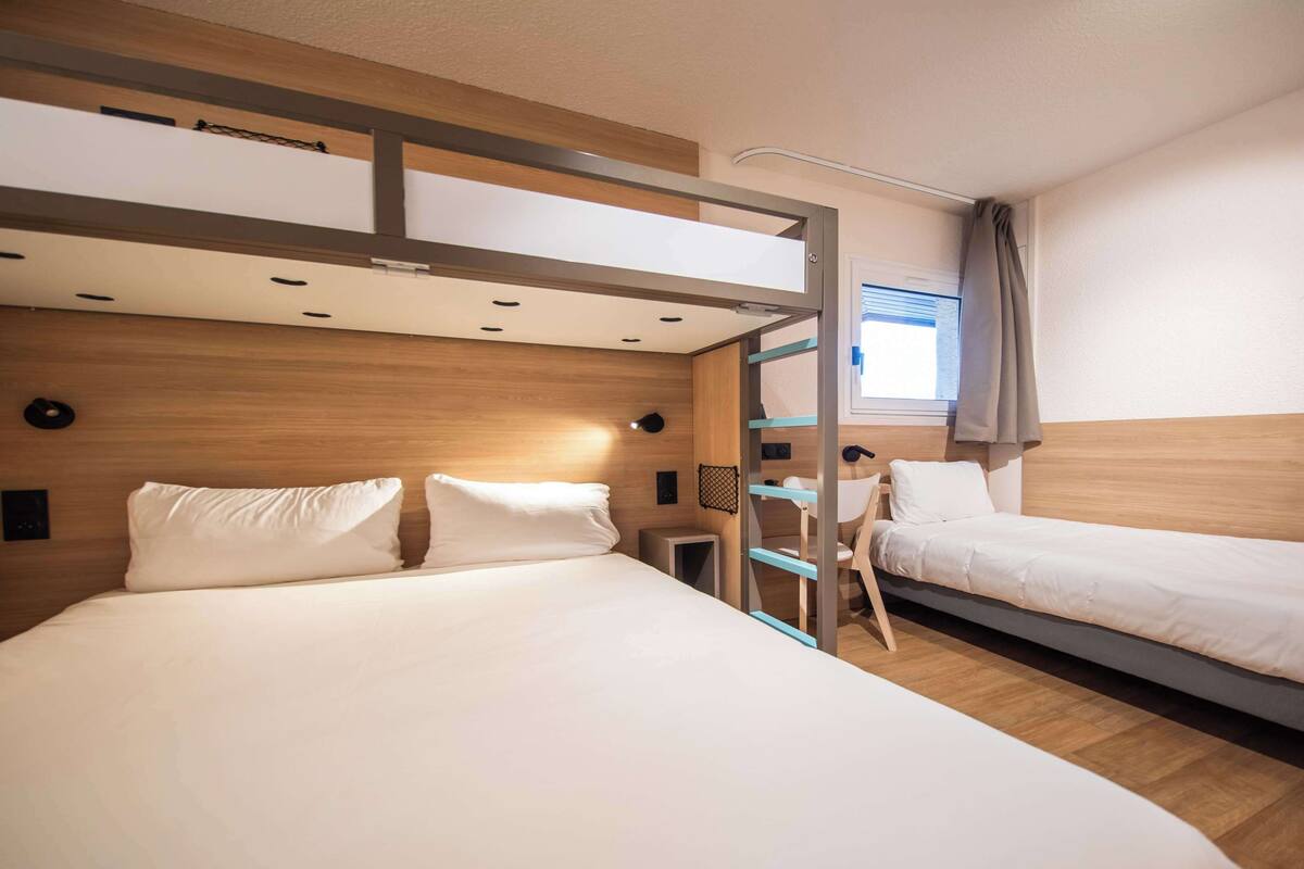 Una habitación de hotel moderna con una cama litera, un escritorio y un ventanal con cortinas.