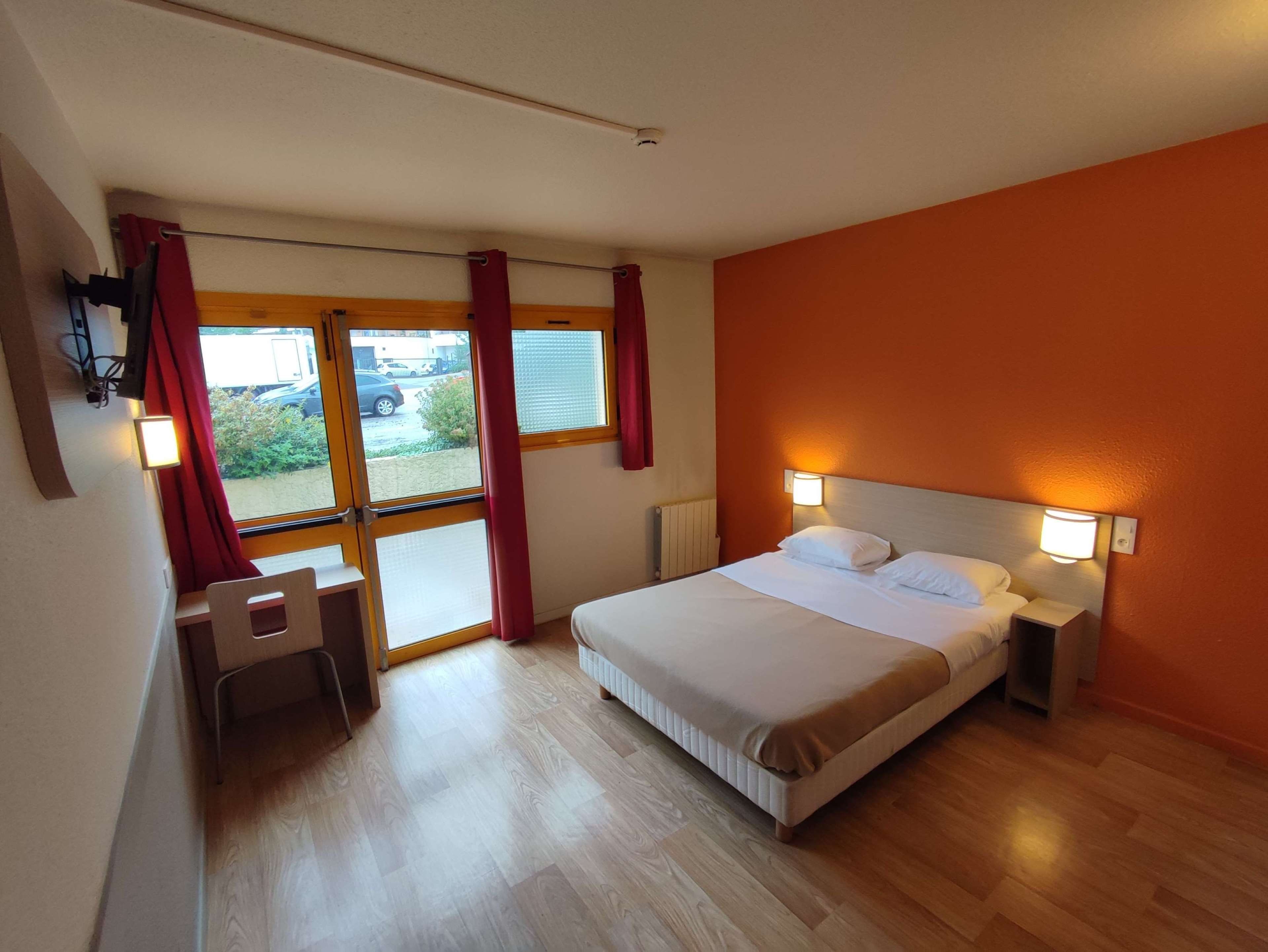 A hotel room with a bed, bedside lamps, a desk, and a view of the outside.