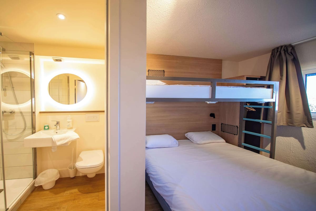 Habitación de hotel compacta con ducha, inodoro y una cama litera.