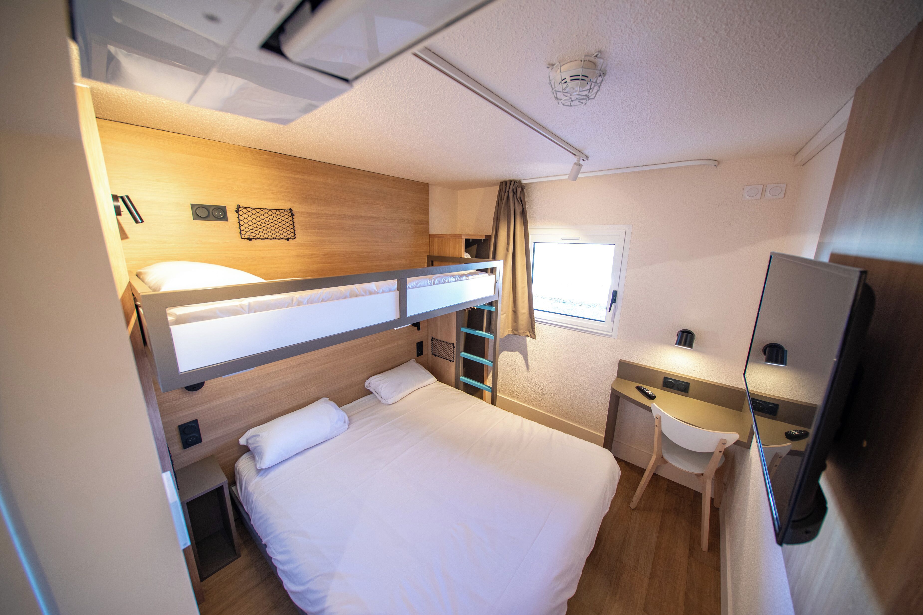 A compact hotel room with a bunk bed, a desk, a chair, and a television.