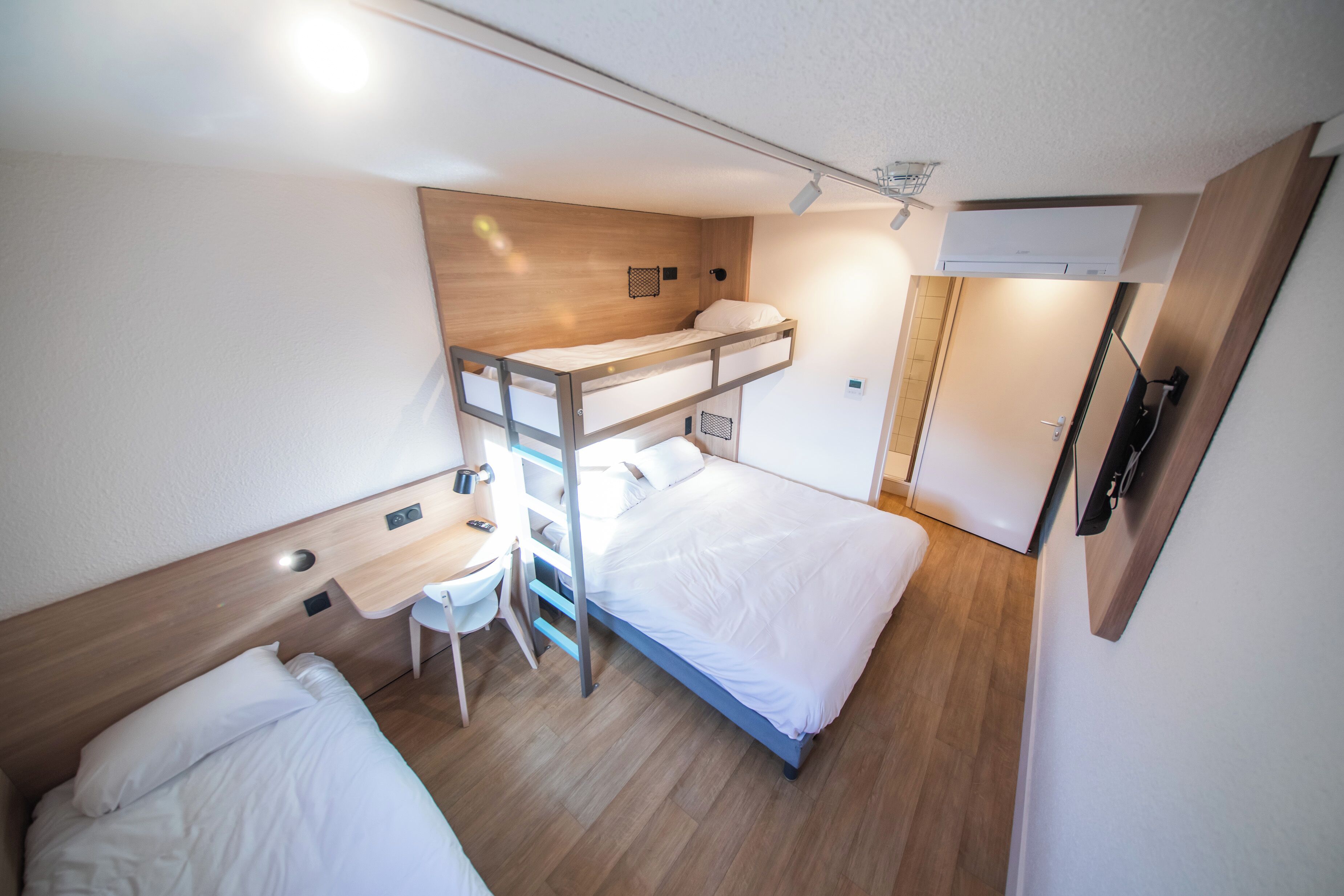 Una habitación de hotel pequeña con literas, un escritorio, una silla y un televisor.