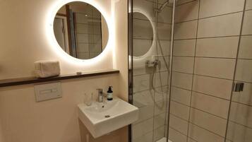 A modern bathroom with a glass-enclosed shower, a round mirror with built-in lighting, a white sink, and a toilet.