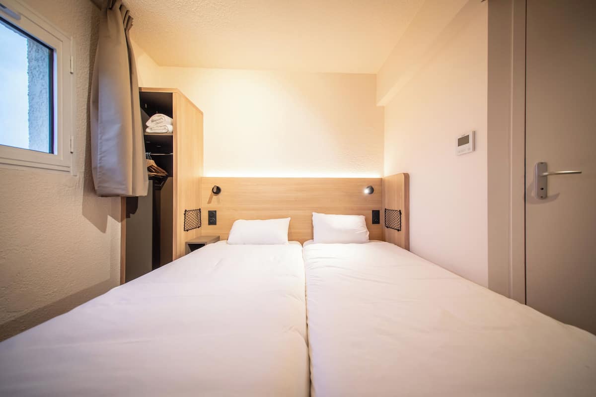 Una habitación de hotel con cama doble, un armario y una ventana pequeña con cortinas.