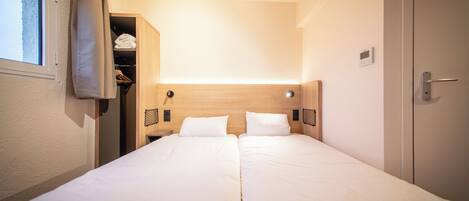 Una habitación de hotel con cama doble, un armario y una ventana pequeña con cortinas.
