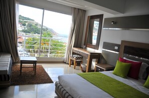 A hotel room with a bed, a desk, a chair, a small table, and a view of a coastal area. - Hotel Marina Prestige Tabarka (Tabarka)