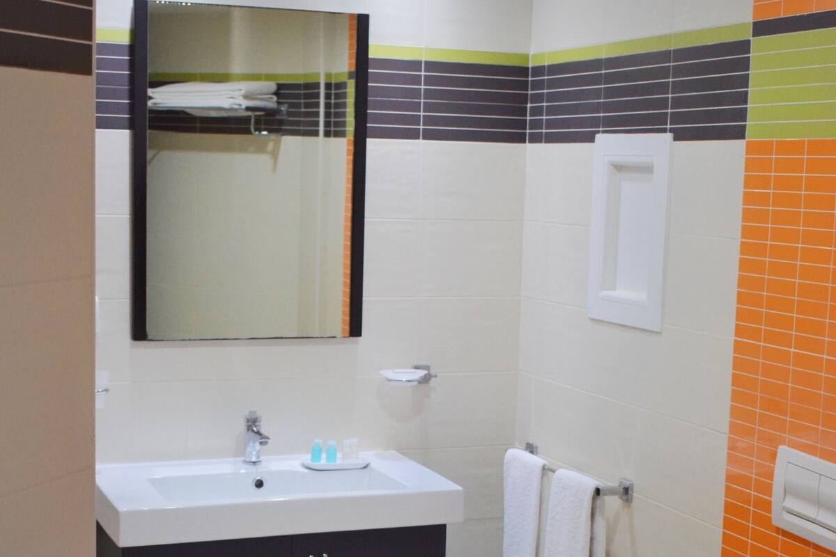 A bathroom with a sink, mirror, toilet, and a small stool.