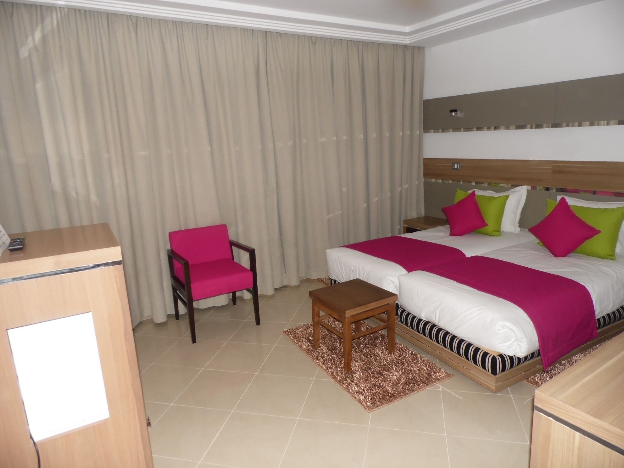 A hotel room with a bed, a desk, a chair, and a large window with curtains.