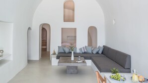 A modern living room with a large sectional sofa, a coffee table, and a dining area with a table set for two. - Pina Caldera Residence (Santorini)