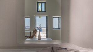 A hotel room with a bed, a chair, a vase, and a view of the outside. - Pina Caldera Residence (Santorini)