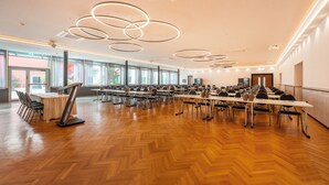 A spacious conference room with a wooden herringbone floor, multiple tables, and chairs. - Hotel Wiehberg (Hannover)