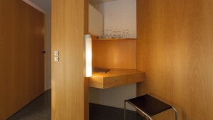 A compact hotel room with a wooden wardrobe, a small desk with a lamp, and a chair. - Hotel Wiehberg (Hannover)