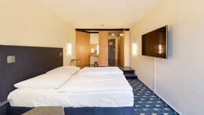 A hotel room with a large bed, a flat-screen TV mounted on the wall, and a small table. - Hotel Wiehberg (Hannover)