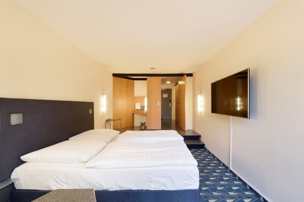 A hotel room with a large bed, a flat-screen TV mounted on the wall, and a small table.