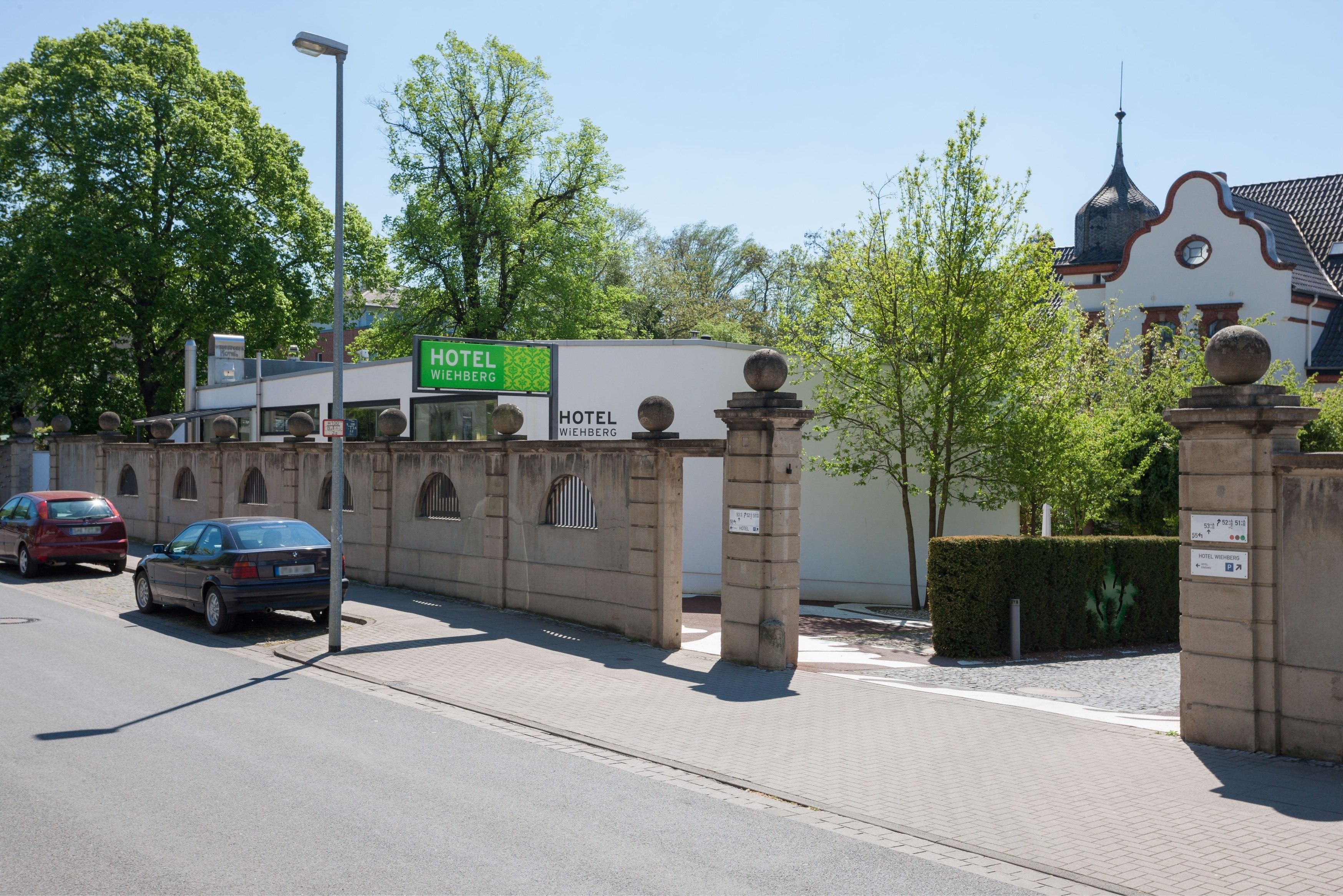 A hotel entrance with a sign, a paved driveway, and a street with parked cars.